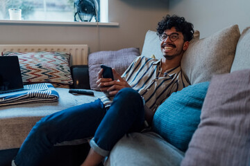 Young Man Resting on a Couch Using His Phone at Home