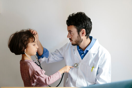 Young doctor examines a child while the kid is allowed to use his stethoscope.