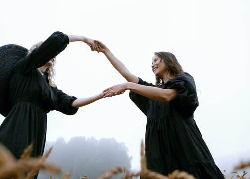 two beautiful girls in black dresses posing dancing in a wheat field
