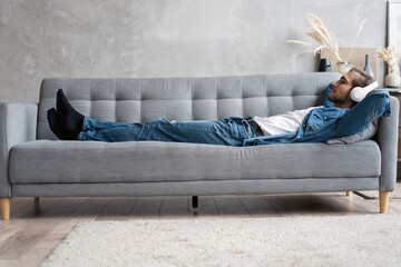 Middle aged man listening music with headphones relaxed in sofa at his home.
