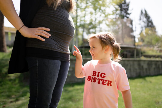 Girl in big sister shirt points at mom's pregnant belly