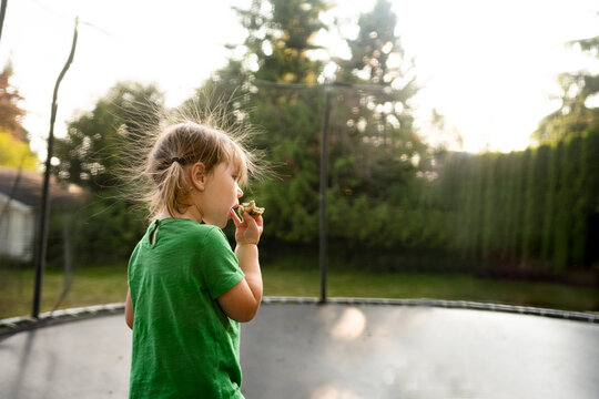 Girl with hair sticking up from static eats on trampoline
