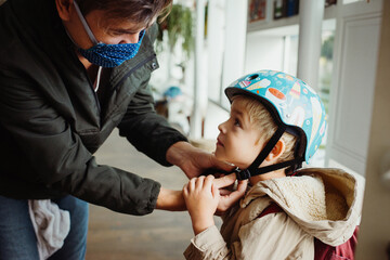 dad wearing a mouth mask helping his son putting on his bicycle helmet
