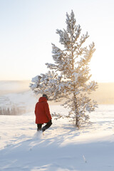 A man in a red jacket walks through the snow to a tree in winter