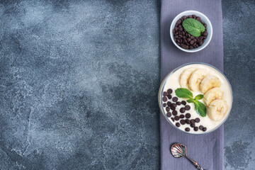 Healthy breakfast, dessert with milk yogurt banana and chocolate on a plate. Dark concrete background. Top view, copy space.