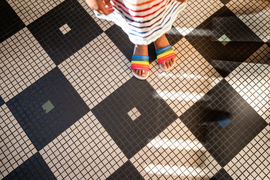 Feet of child in rainbow sandals on tile floor
