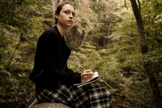 Young woman sitting and drawing in notebook in forest during autumn