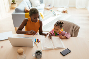 Black working mother doing homework with daughter