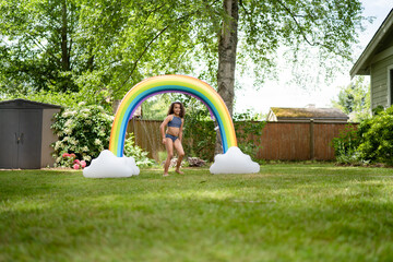 Wide shot of curly haired girl in back yard rainbow sprinkler