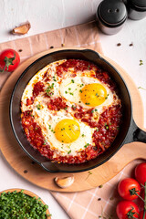 Flat lay image of shakshouka in a pan on a light coloured background