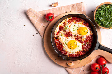 Flat lay image of shakshouka in a pan on a light coloured background