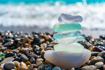 Sea glass stones arranged in a balance pyramid on the beach. Beautiful azure color sea with blurred seascape background. Meditation and Harmony concept.