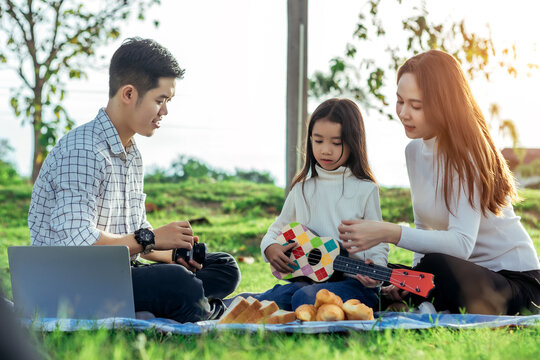 Happy asian family in the garden They play ukulele, singing, take pictures by film camera, eat together and have fun.