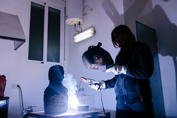 Woman sculptor welding a piece in her studio