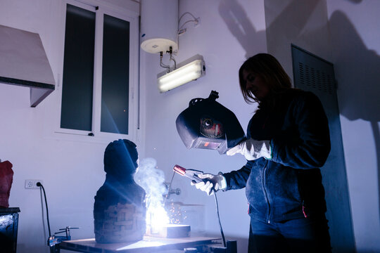 Woman sculptor welding a piece in her studio