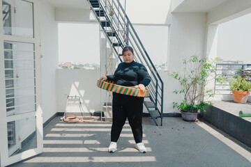 Plus size young asian woman playing hula hoop in balcony. Helps to burn excess fat in body....