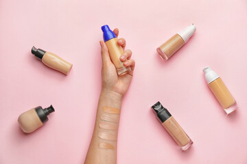 Female hand with bottles of makeup foundation and samples on color background