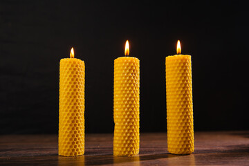 Three yellow beeswax candles are on the table. - obrazy, fototapety, plakaty