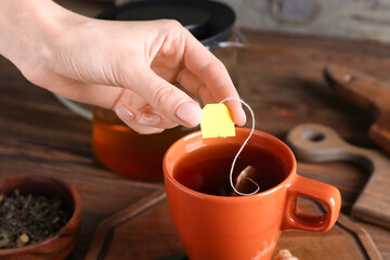 Woman dipping tea bag into cup on wooden background