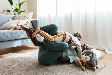 Ethnic mother with little kid playing in living room