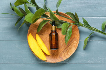 Plate with bottle of mango essential oil on color wooden background