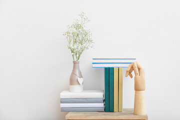 Shelf unit with books, vase and wooden hand  against light wall in room