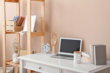 Stylish workplace with laptop and shelf unit against color wall in room