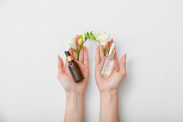Female hands with cosmetic products and beautiful flowers on light background