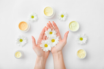 Female hands with jars of cream and beautiful flowers on light background