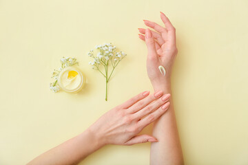 Female hands with jar of cream and beautiful flowers on color background