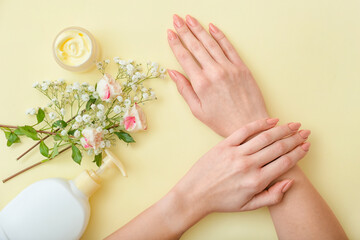 Female hands with cosmetic products and beautiful flowers on color background