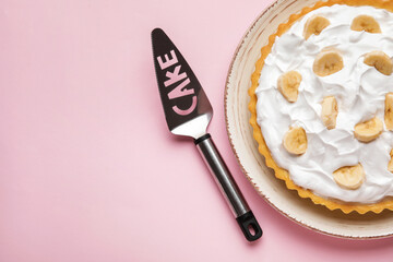 Plate with tasty banana pie and spatula on color background