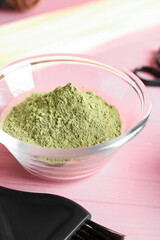 Bowl with henna and hair comb on color wooden background, closeup