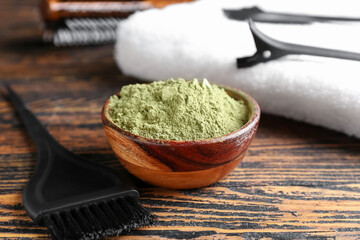 Bowl with henna and hairdresser's supplies on dark wooden background, closeup