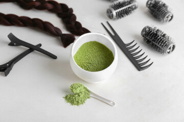 Bowl with henna, braided strand and hairdresser's supplies on light background