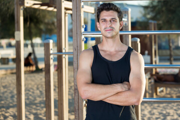 Fototapeta na wymiar Lifestyle portrait of muscular man in sportswear near fitness station on beach