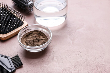 Bowl with henna, hairdresser's supplies and glass of water on color background
