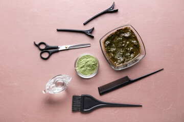 Bowls with henna and hairdresser's supplies on color background
