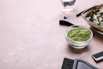 Bowls with henna and hairdresser's supplies on color background