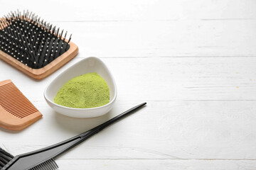 Bowl with henna and hair combs on white wooden background