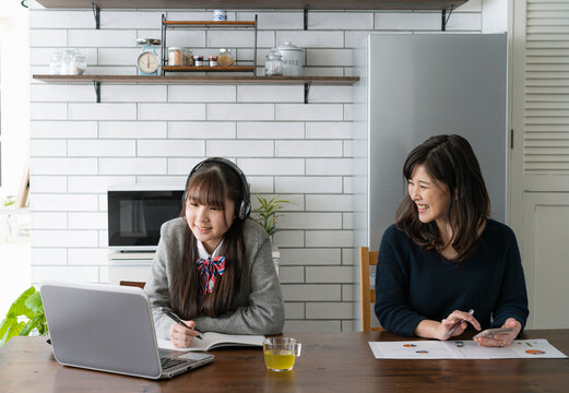 自宅でオンライン学習をする日本人女子学生と仕事をする母親