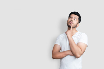 Asian handsome man on white t-shirt having doubts while looking up over isolated white background