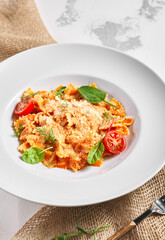 Farfalle pasta food on white table. Pasta restaurant plate with basil leaf and tomato, red tomato sauce. Delicious italian pasta.