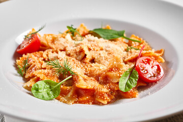 Farfalle pasta food on white table. Pasta restaurant plate with basil leaf and tomato, red tomato sauce. Delicious italian pasta.