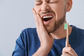 Man with aching teeth and brush on grey background