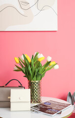 Bouquet of spring flowers and female bags on table in modern hallway