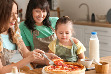Young woman with her little daughter and mother eating pizza at home