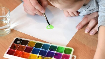 Dad and son drawing a green leaf of clover on a white sheet of paper with paintbrush and watercolors.Hands close up.Concept of St.Patrick's Day.Joint family leisure.