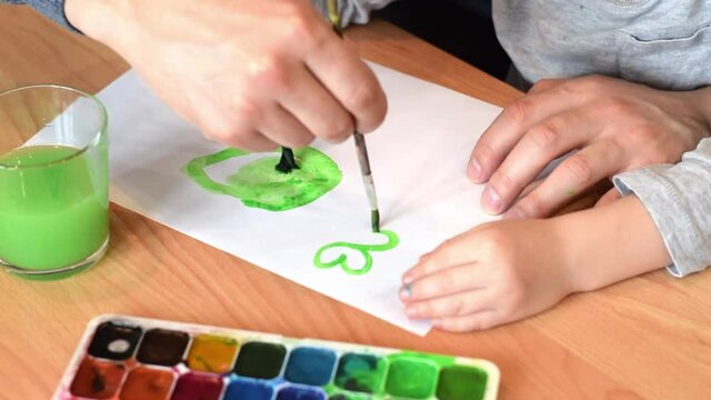 Dad and son drawing a leaf of clover on a white sheet of paper with paintbrush and watercolors.Hands close up.Concept of St.Patrick's Day.Joint family leisure.