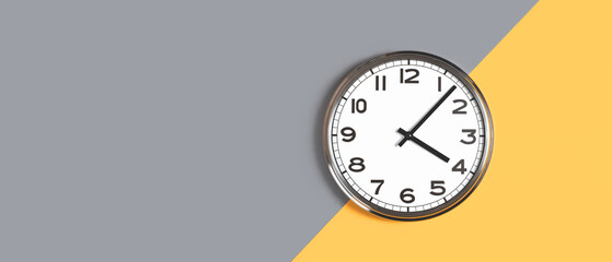 Plain wall clock in the center of grey and orange background. Four o'clock. Close up banner with...
